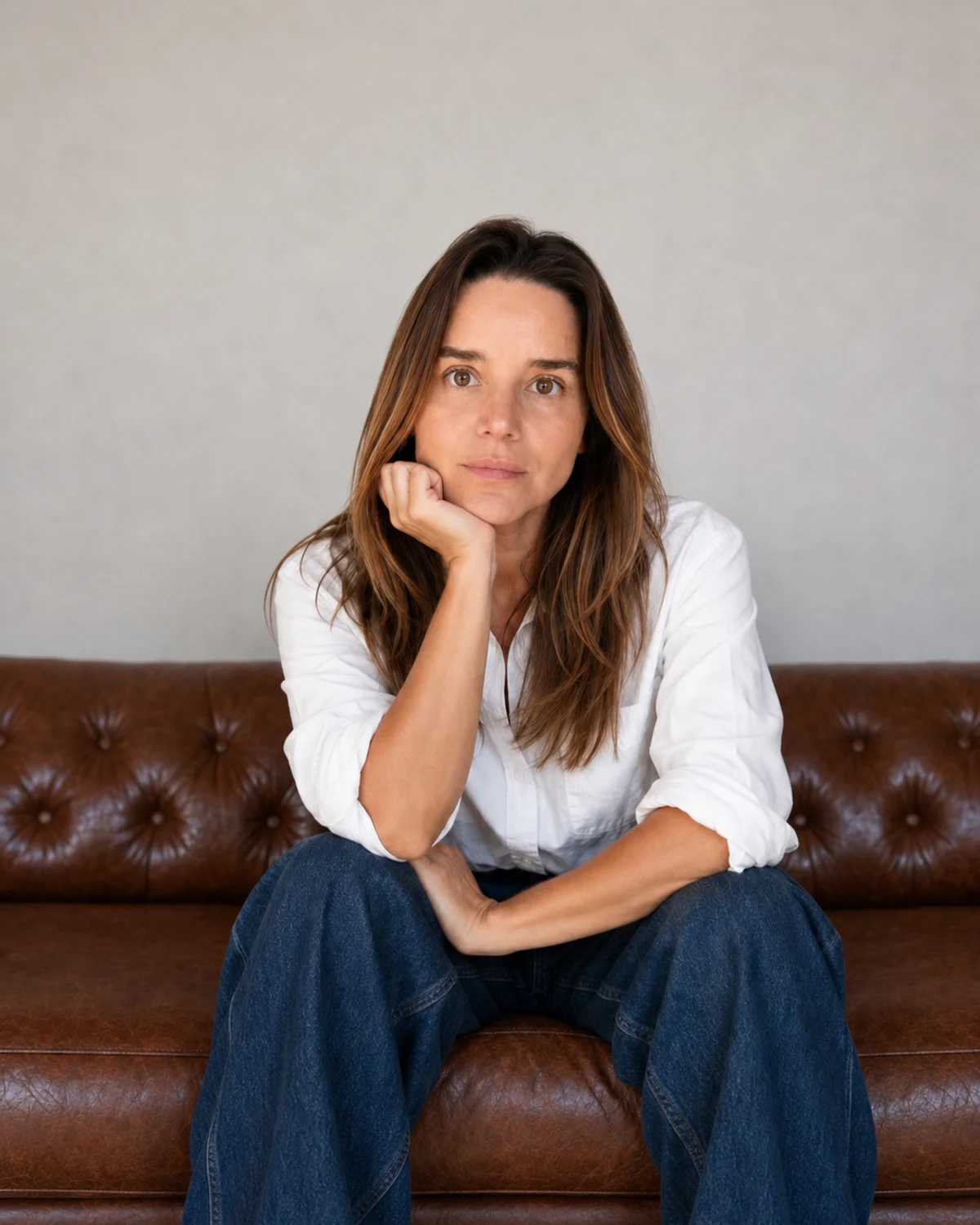 Vanessa Caldas sentada em um sofá de couro, usando camisa branca